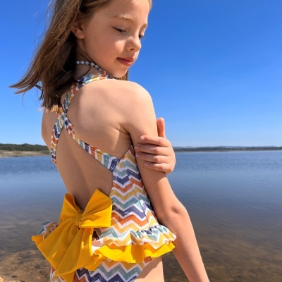 Fato de banho infantil colorido com laço amarelo, menina ao ar livre junto à praia