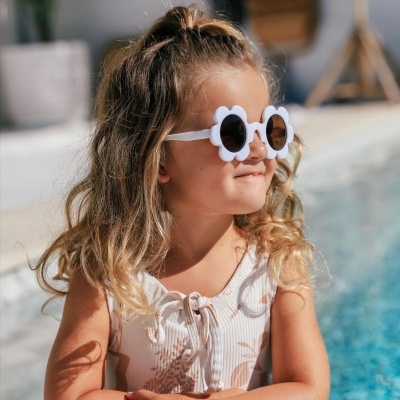 Criança com óculos de sol floridos brancos ao lado de piscina