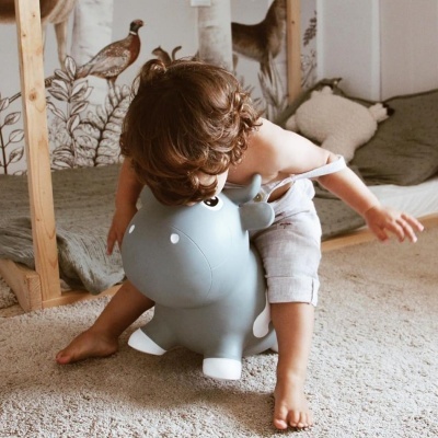 Criança sentada em brinquedo insuflável cinzento num quarto com decoração de animais