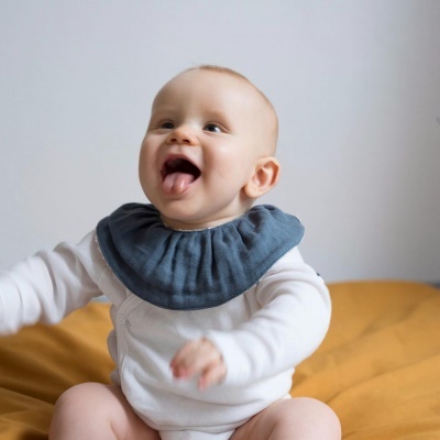 Bebé com babete azul-escuro sentado em tecido amarelo