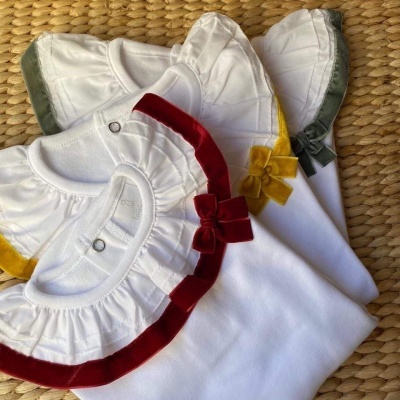 Três bodies de bebé brancos com gola franzida e laços de veludo em vermelho, amarelo e verde