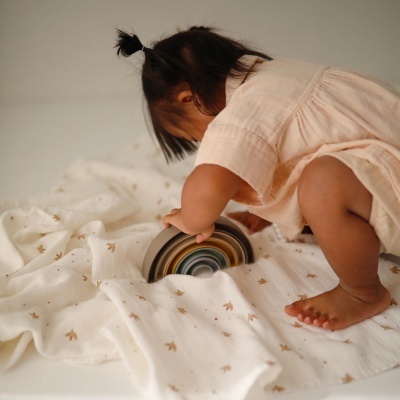 Bebé sentado brincando com brinquedo arco-íris em pano branco com desenhos