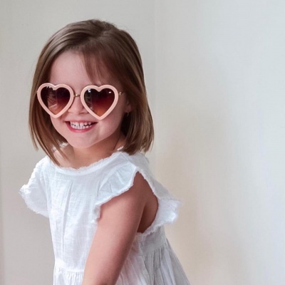Criança com óculos de sol rosa em forma de coração e vestido branco