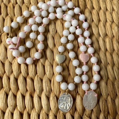 Duas pulseiras com contas brancas, corações coloridos e medalhas metálicas sobre fundo trançado