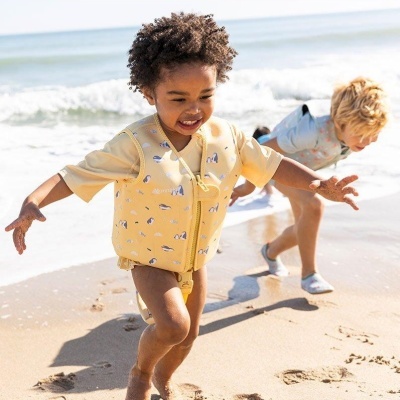 Criança na praia com colete amarelo de patinhos