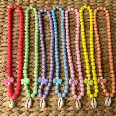 Colares coloridos de contas com borboleta e concha sobre superfície trançada