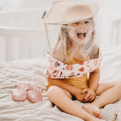 Criança com saco mosquiteiro rosa sentado em cama com sapatos transparentes cor-de-rosa ao lado