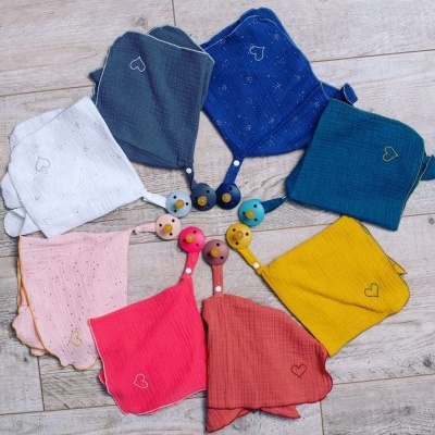 Oito panos coloridos com pequenos corações bordados e pinças coloridas, dispostos em círculo sobre chão de madeira clara