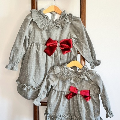 Dois vestidos infantis cinza com bolinhas e laço vermelho pendurados numa escada de madeira