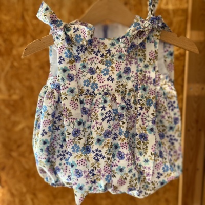 Roupa infantil floral branca com laços pendurada em cabides de madeira