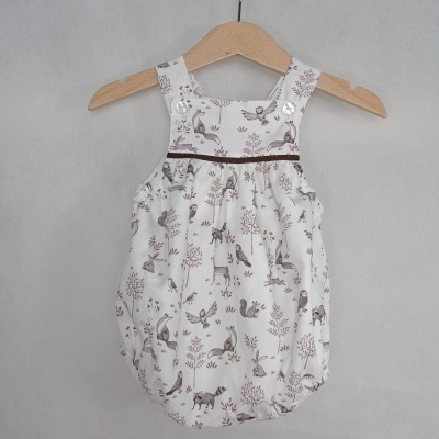 Macacão de bebé branco com padrão de animais castanhos em cabide de madeira