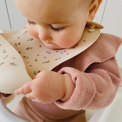 Babete de silicone floral com bebé de camisola rosa sentado