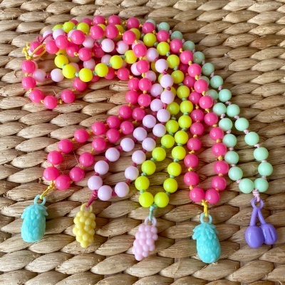 Brincos coloridos de contas com pendentes de frutas sobre superfície de palha