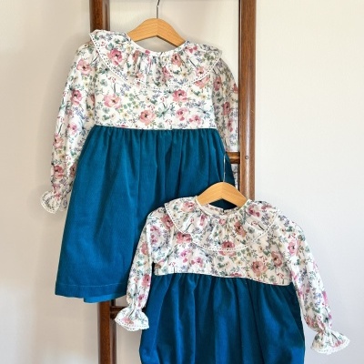 Dois fatos de bebé em padrões florais e azul turquesa pendurados numa estrutura de madeira