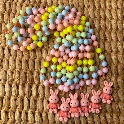 Colares infantis com contas coloridas e pendentes de coelhinho cor-de-rosa sobre superfície trançada