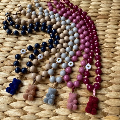 Colares coloridos com pendentes em forma de ursinho em veludo sobre superfície de palha