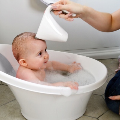 Bebé numa banheira branca a ser lavado com jarro branco
