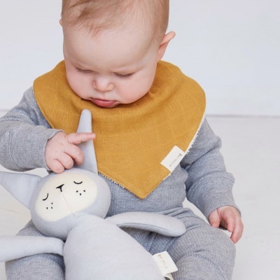 Bebé com macacão cinzento e babete amarelo segurando boneco de peluche cinzento