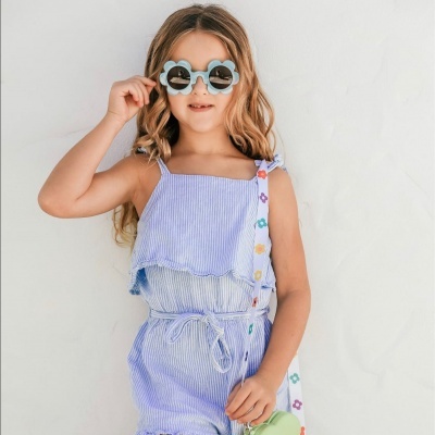 Criança com macacão azul às riscas e óculos de sol em fundo branco