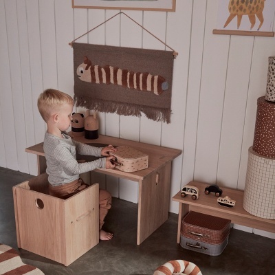 Menino numa cadeira de madeira junto a secretária de madeira clara em quarto infantil decorado.