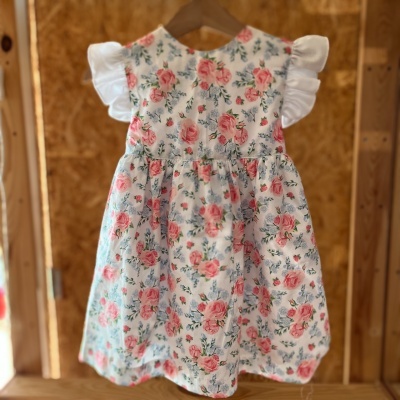 Vestido de bebé com padrão floral rosa e verde em fundo branco e mangas folhadas brancas