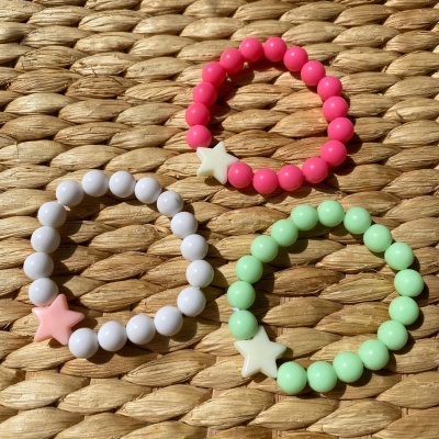 Três pulseiras de contas coloridas com estrelas sobre superfície trançada