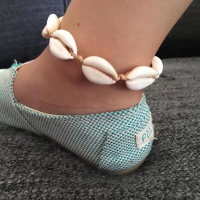 Pulseira de búzios brancos no tornozelo com meia sapatilha azul e carpete cinza