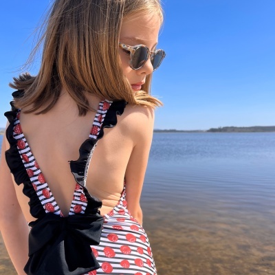 Menina de costas com fato de banho às riscas e óculos de sol junto a água