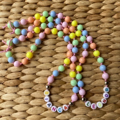 Colares coloridos com contas plásticas e nomes BIANCA e LEONOR em contas brancas sobre tecido natural