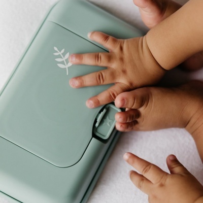 Fraldas reutilizáveis verdes com desenho de folha branco e mãos de bebé.