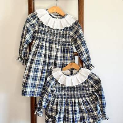 Dois vestidos infantis xadrez com gola branca pendurados numa estrutura de madeira