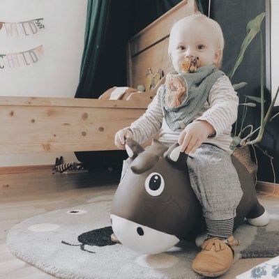 Bebé sentado numa mota insuflável forma de touro castanha em quarto com cama madeira clara.
