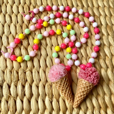 Colar colorido com pendentes em forma de cones de gelado cor-de-rosa sobre superfície tecida.