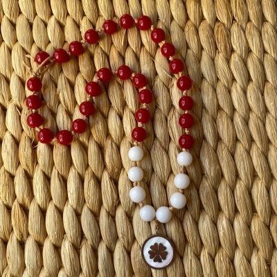 Colar com contas vermelhas e brancas e pendente de trevo sobre tecido trançado bege