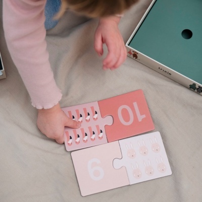 Peças de puzzle cor-de-rosa com números 9 e 10 e desenhos de animais, mão de criança a segurá-las.