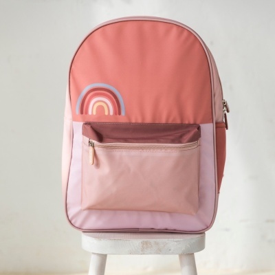 Mochila rosa com bolso frontal e arco-íris sentada num banco branco
