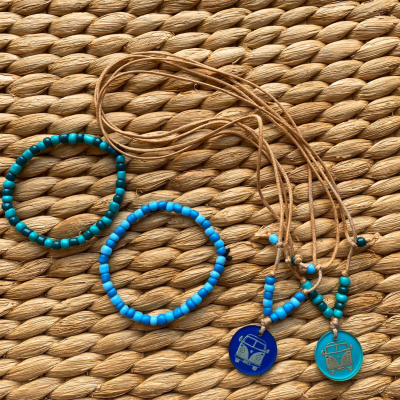Colares com pendentes de carrinha e pulseiras de contas azuis e verdes sobre superfície de corda trançada.