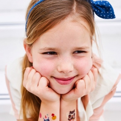 Criança com fita de cabelo azul com bolinhas e tatuagens temporárias coloridas nos braços