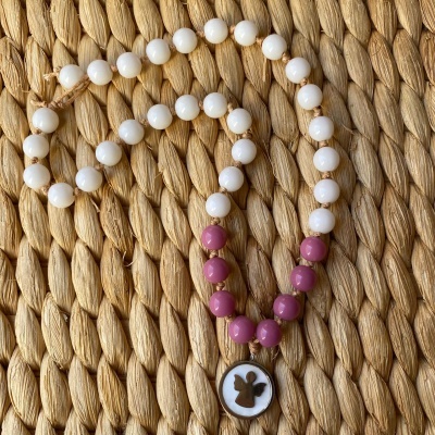 Colar com contas brancas e rosas com pendente de anjo sobre superfície de ráfia