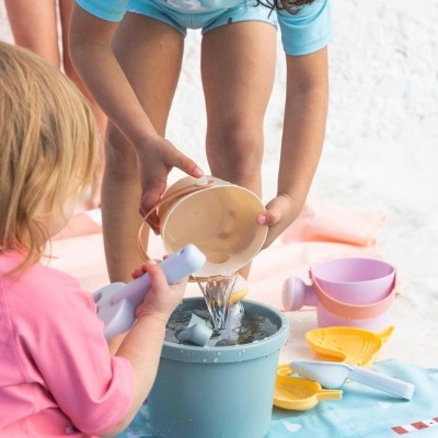 Crianças a brincar com baldes e pás de plástico coloridos, despejando água de um balde para outro.