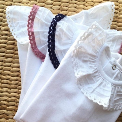 Bodies de bebé brancos com golas rendadas coloridas, sobre tecido trançado natural