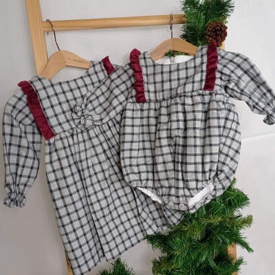 Dois vestidos infantis xadrez cinza e branco com detalhes em veludo vermelho pendurados em cabides