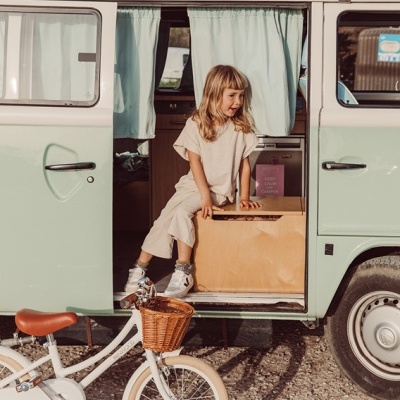Criança numa caixa dentro de carrinha clássica verde e branco com bicicleta branca à frente