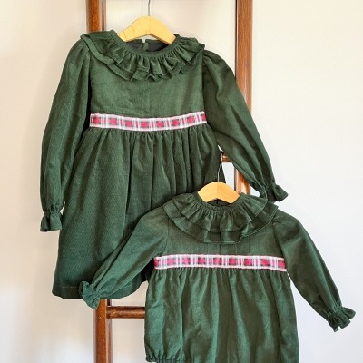 Conjunto infantil verde com gola franzida e faixa xadrez branco e vermelho pendurado numa escada de madeira.