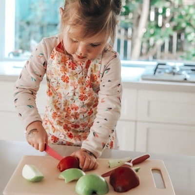 Criança a cortar maçãs com faca numa tábua de corte numa cozinha branca