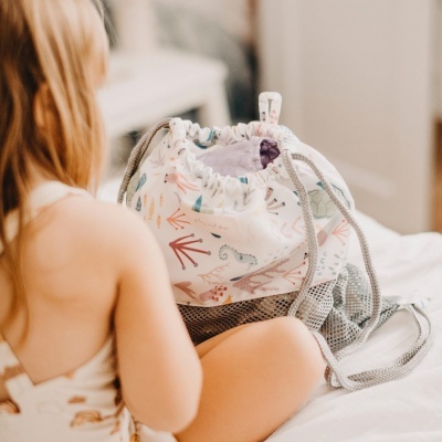 Mochila saco para criança com padrão colorido junto a criança numa cama