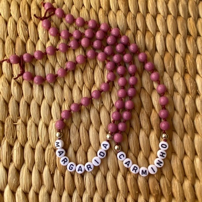 Colares com contas cor-de-rosa e nomes em letras brancas sobre superfície de fibra natural