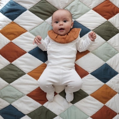 Bebé de macacão branco e babete castanho sobre tapete acolchoado colorido