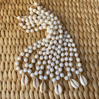 Colar com contas brancas e conchas sobre tecido trançado bege