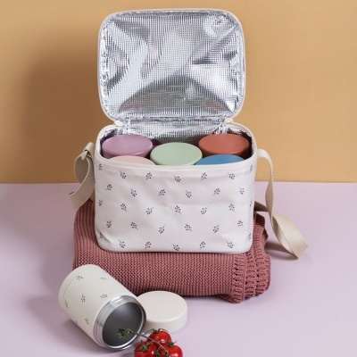 Bolsa térmica branca com padrão pequeno de folhas, recipiente colorido dentro, junto a tomate cereja e tubo branco